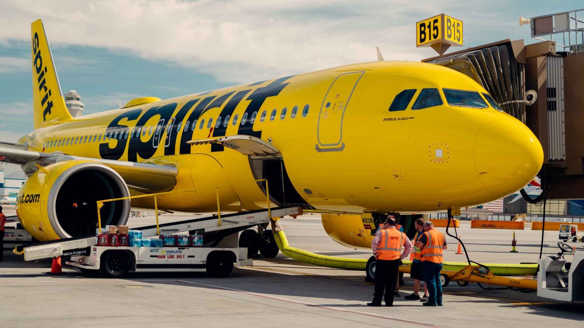 Spirit Airlines yellow Airbus A320 at gate B15 with ground crew preparing flight