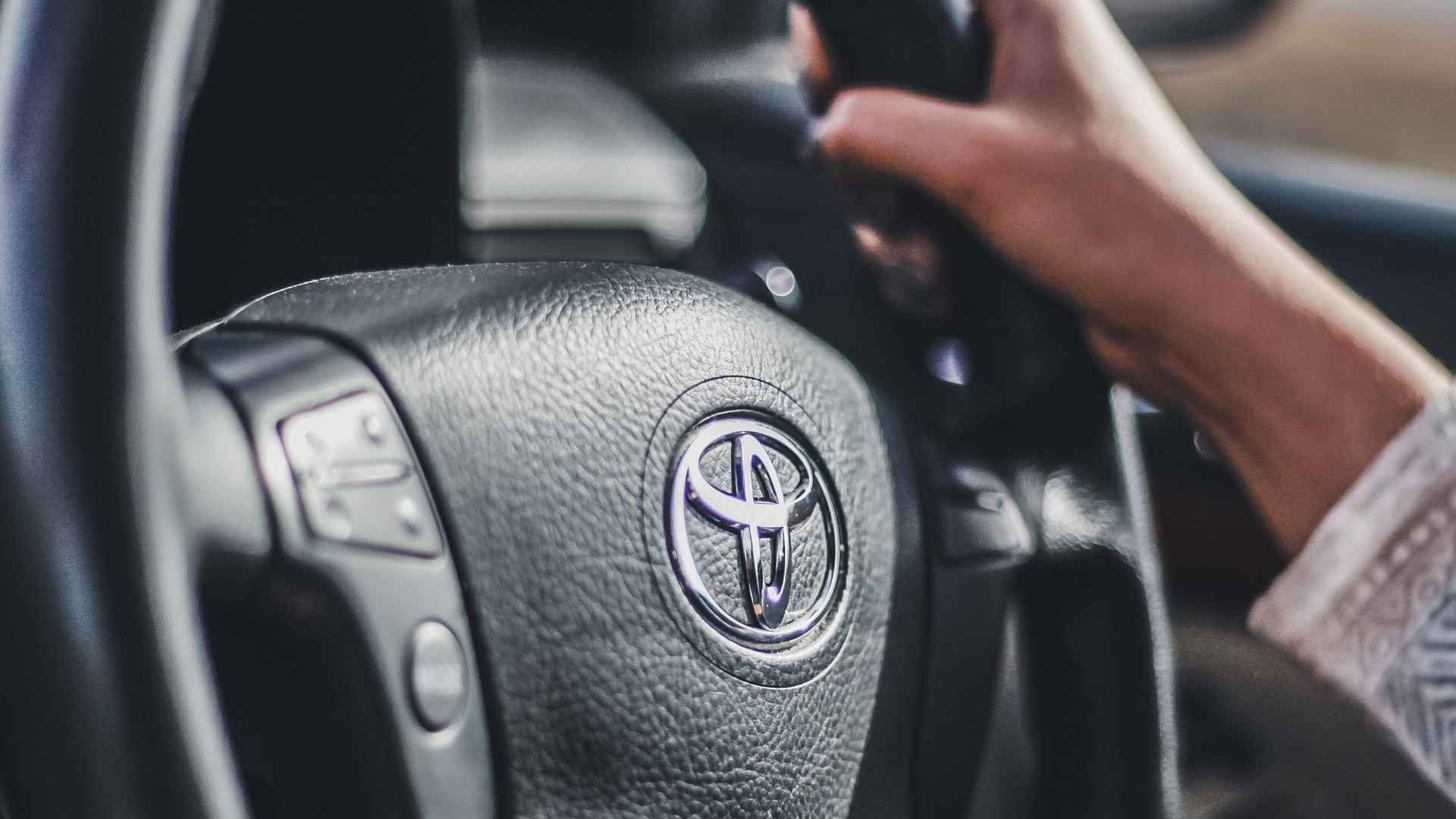 Close-up of a Toyota steering wheel held by a driver's hand, representing warranty claim denial.