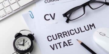 Documentos de currículum vitae sobre un escritorio con gafas, teclado, reloj y lápiz, representando la importancia de preparar un CV profesional