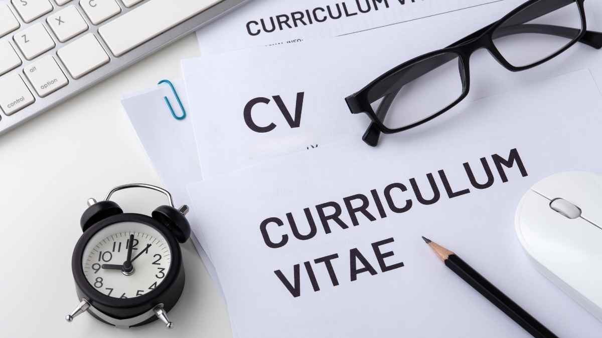 Documentos de currículum vitae sobre un escritorio con gafas, teclado, reloj y lápiz, representando la importancia de preparar un CV profesional