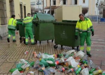 Trabajadores de limpieza urbana recogiendo basura en la calle cerca de contenedores verdes