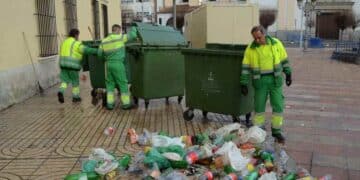 Trabajadores de limpieza urbana recogiendo basura en la calle cerca de contenedores verdes