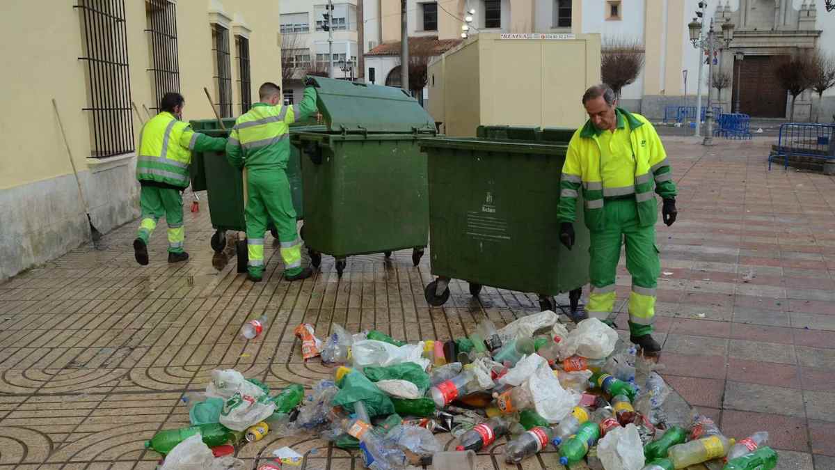 Trabajadores de limpieza urbana recogiendo basura en la calle cerca de contenedores verdes