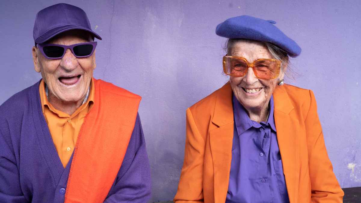 Pareja de jubilados sonrientes con ropa colorida en tonos naranjas y morados, representando una jubilación feliz en 2025