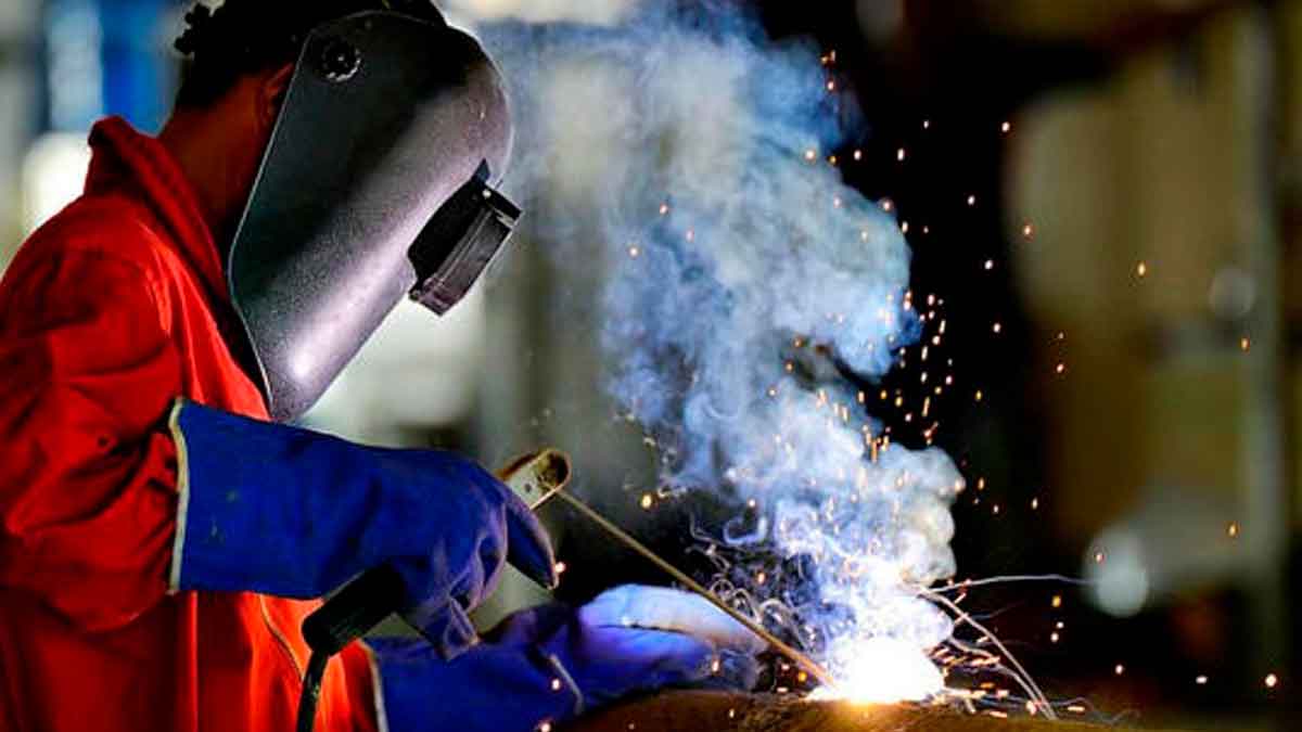 Soldador trabajando con equipo de protección en una fábrica de metalurgia