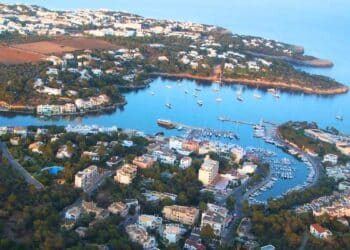 Vista aérea de un pueblo costero en Mallorca con puerto y viviendas rodeadas de naturaleza, donde se ofrecen empleos de vigilante de seguridad