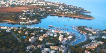 Vista aérea de un pueblo costero en Mallorca con puerto y viviendas rodeadas de naturaleza, donde se ofrecen empleos de vigilante de seguridad