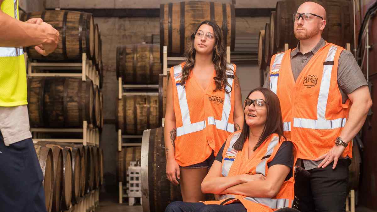 Tres trabajadores con chalecos reflectantes y gafas de seguridad en un almacén de barriles