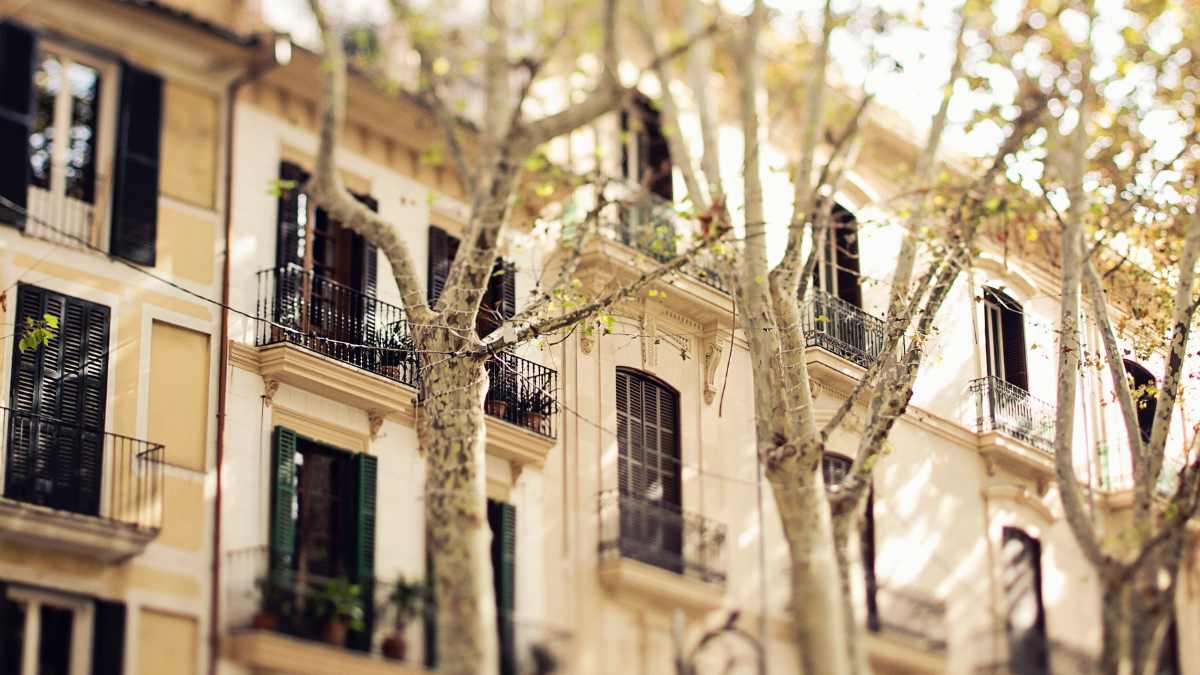 Fachadas de viviendas con balcones y árboles en una calle, representando segundas residencias en España