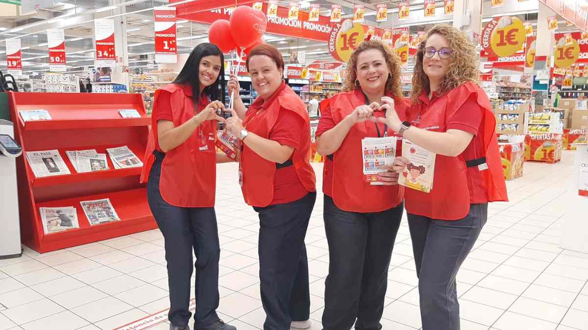 Empleadas de Alcampo con uniforme rojo formando corazones con las manos en un supermercado de España