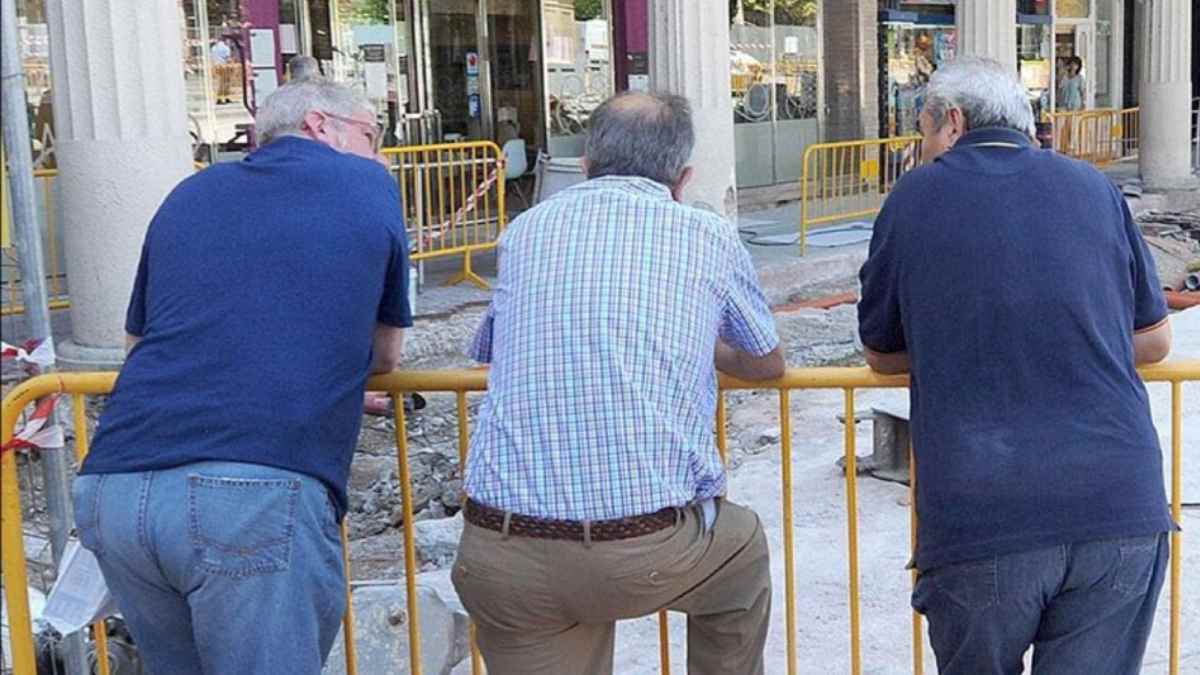 Trabajadores nacidos entre 1960 y 1970, cerca de la jubilación, apoyados en una valla en la vía pública