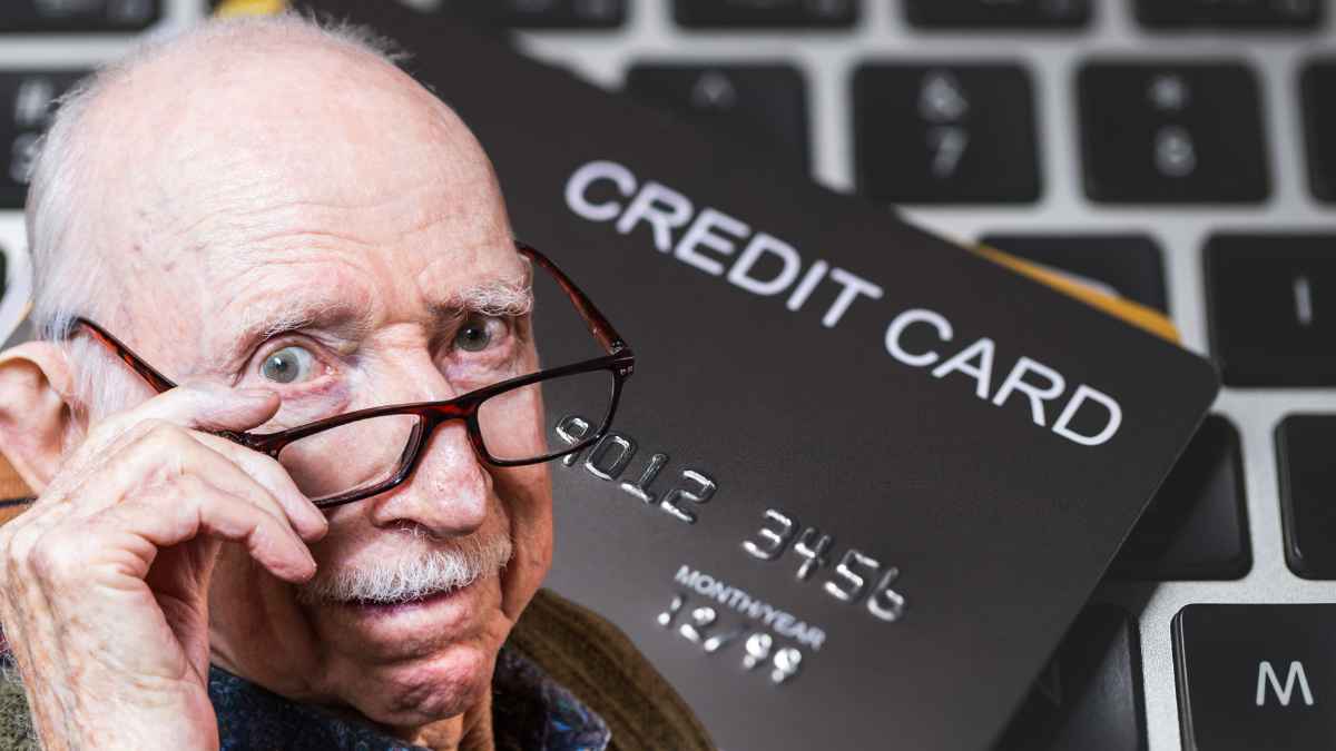 Hombre mayor con expresión preocupada sostiene gafas frente a tarjeta de crédito sobre teclado, simbolizando deudas en mayores de 55 años