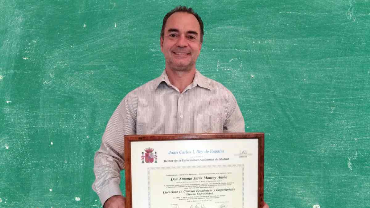 Hombre con diploma posando ante pizarra verde tras lograr 13 carreras y 2 doctorados