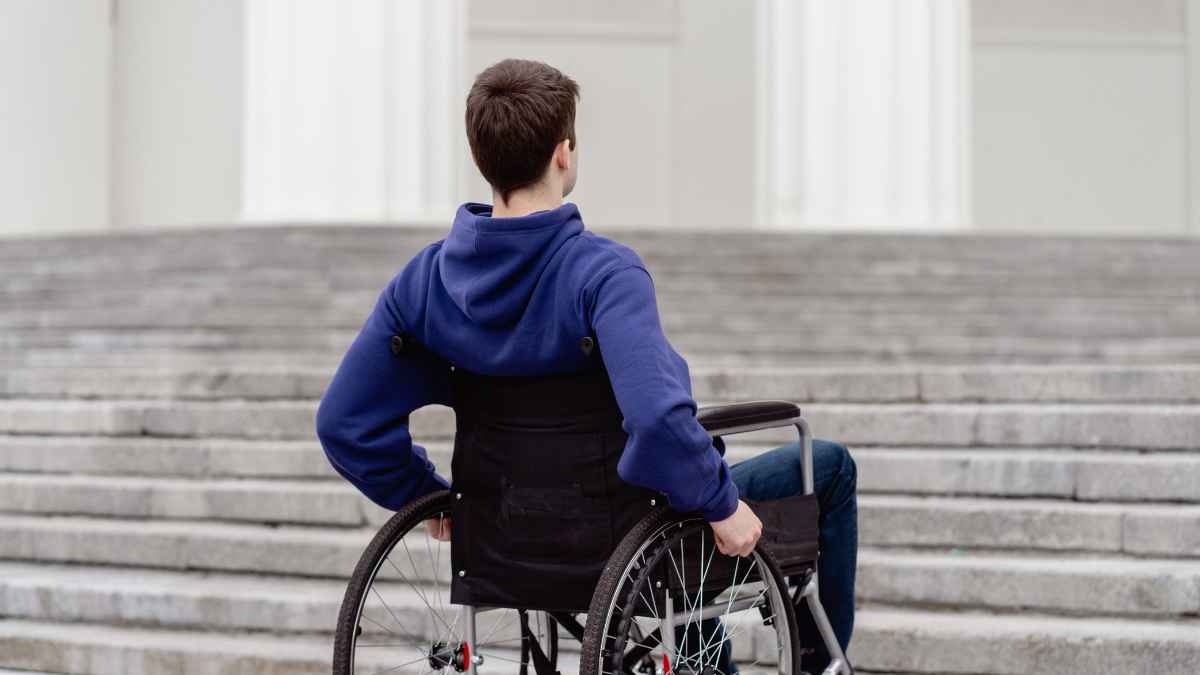Hombre en silla de ruedas frente a las escaleras del INSS para revisión de pensiones de incapacidad