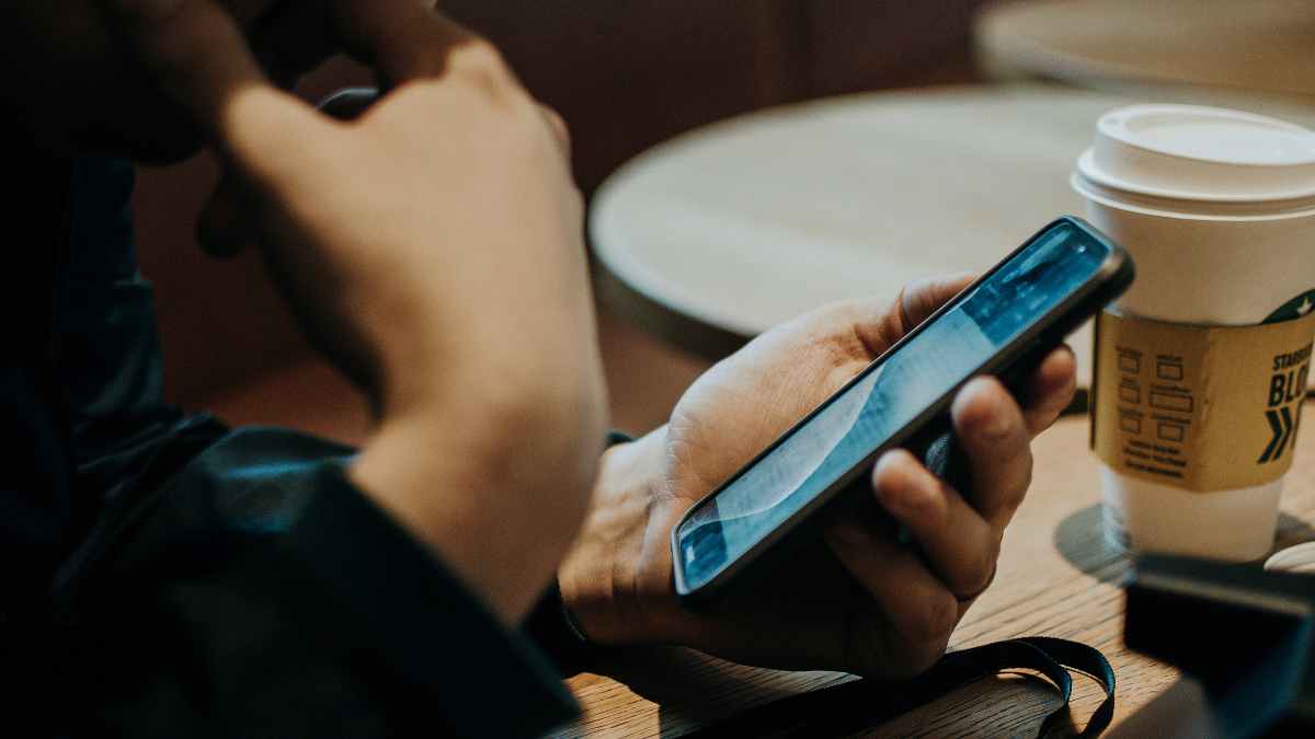 Manos sujetando smartphone junto a taza de café simbolizando consentimiento previo para llamadas spam según la OCU