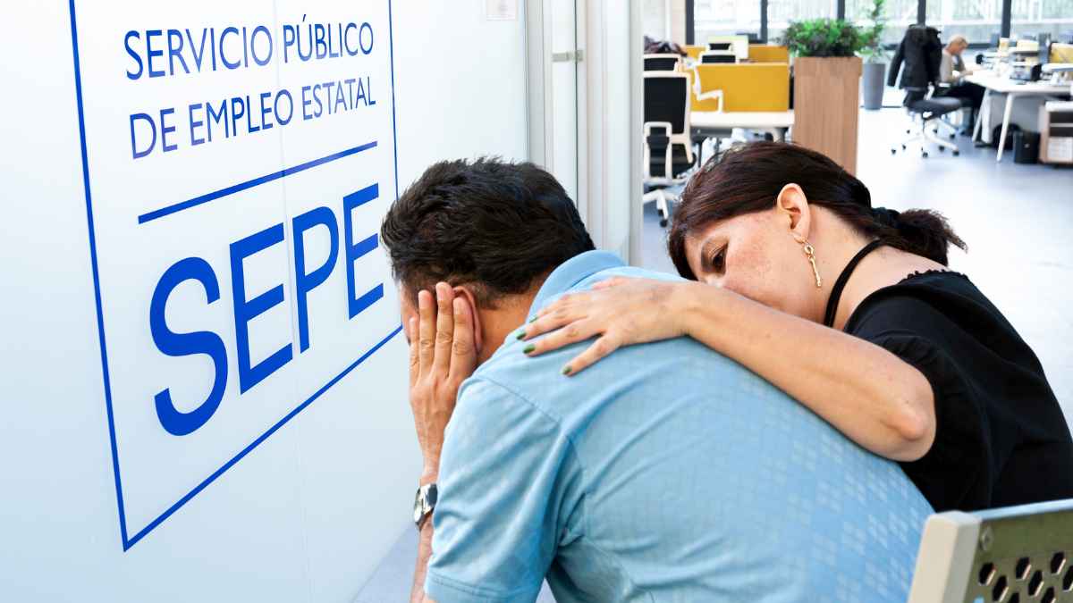 Hombre preocupado en una oficina del SEPE, consolado por una compañera, que refleja el impacto de reducir el paro tantos días como dura la baja tras el despido.