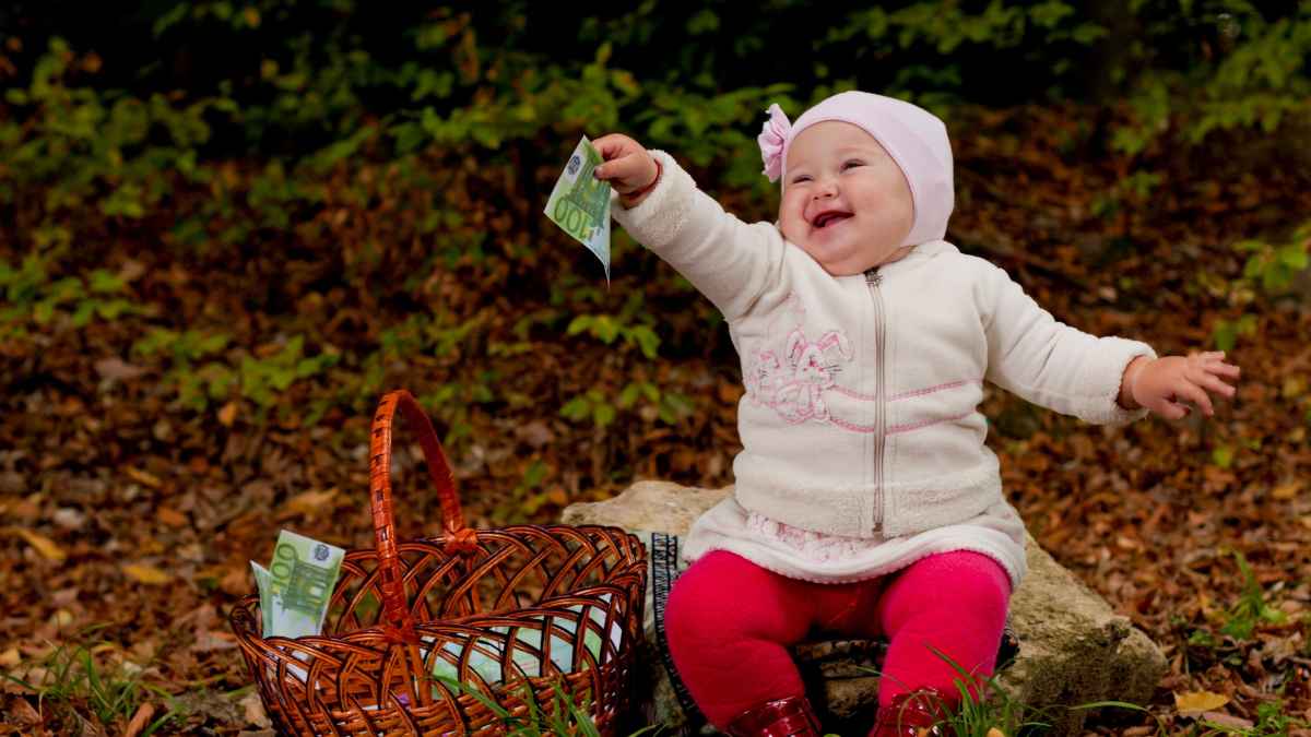Bebé sonriente con billete de 100 € que ilustra la ayuda de hasta 1.000 euros por nacimiento en Madrid 2025