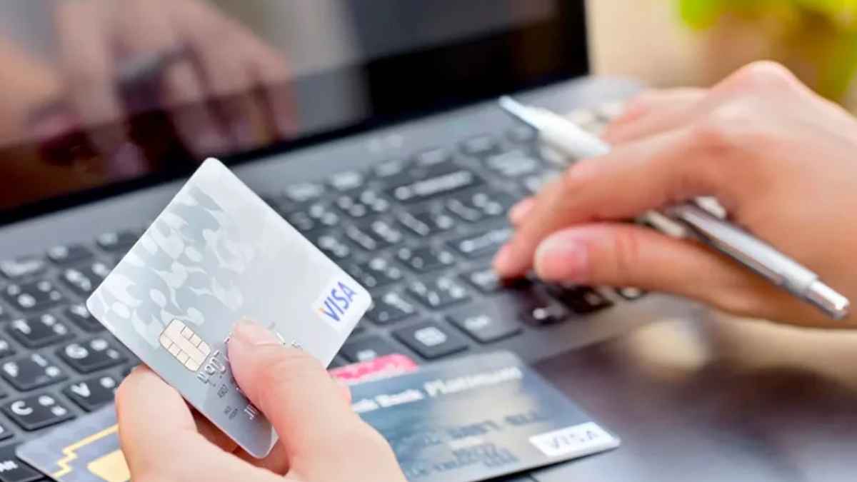 Mano con tarjeta Visa sobre portátil realizando transferencia online; alerta Banco de España por estafas en alquileres