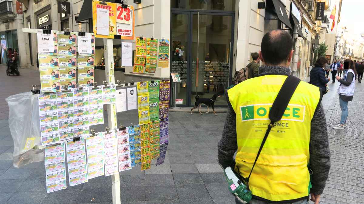 Vendedor de la ONCE con chaleco amarillo ofreciendo cupones y rascas en una calle peatonal de España en 2025