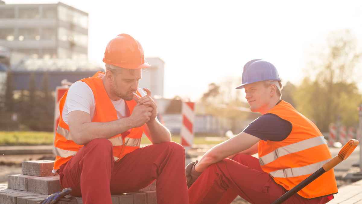 Dos trabajadores de la construcción descansan con chaleco y casco durante la pausa de 15 minutos que garantiza el Estatuto de los Trabajadores