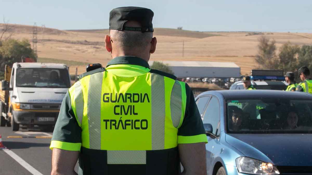 Agente de la Guardia Civil de Tráfico de espaldas inspeccionando un vehículo en un control de carretera.