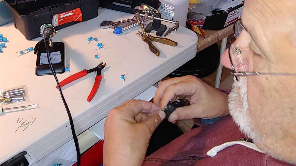 Jubilado de 77 años ensamblando un mini-generador que convierte bolsas de plástico en electricidad barata sobre su mesa de trabajo