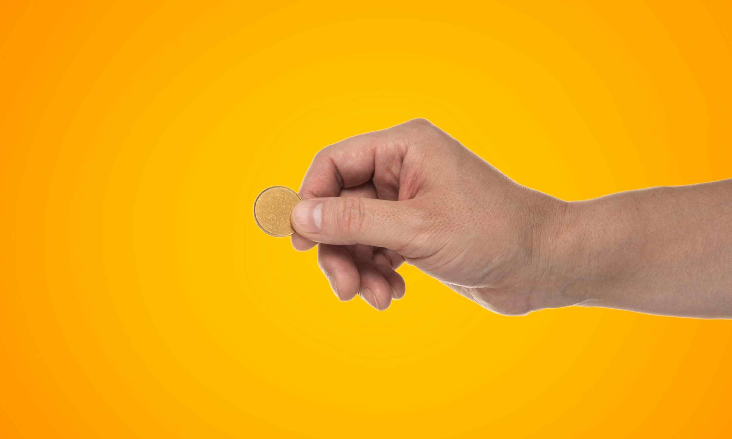 Mano sujetando una moneda valiosa de un centavo sobre fondo amarillo