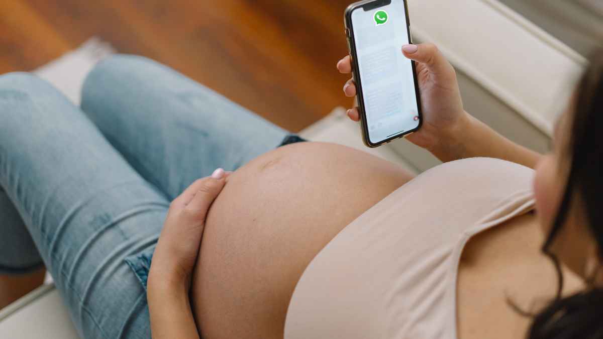 Mujer embarazada acaricia su barriga mientras revisa un chat de WhatsApp en el móvil, clave en su despido e indemnización