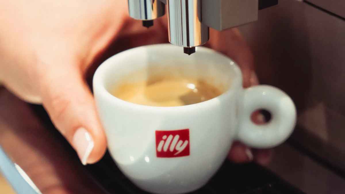 mano sosteniendo taza de café espresso bajo cafetera en una oficina, pausa café laboral