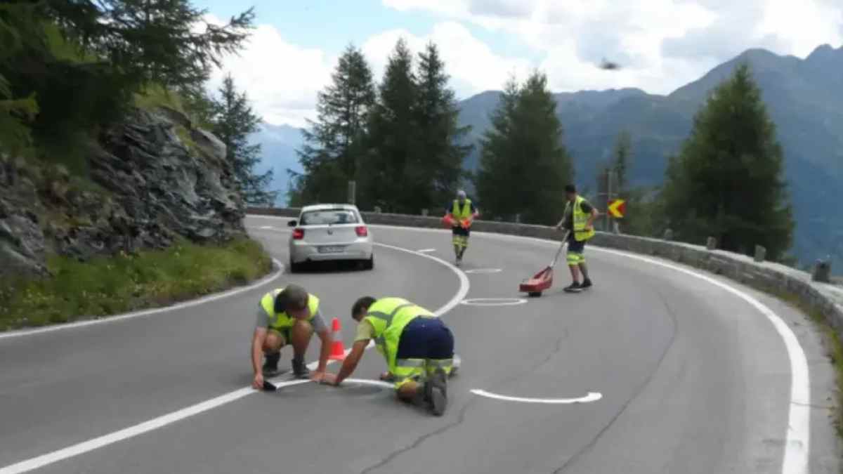 Trabajadores pintan círculos reflectantes en curva de montaña para guiar a motoristas y evitar colisiones frontales