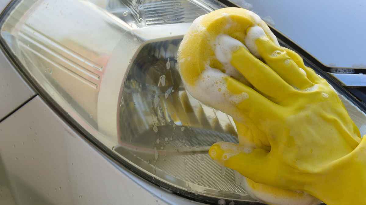 Mano con guante amarillo aplicando espuma y algodón mágico de Mercadona sobre el faro de un coche para restaurar su brillo
