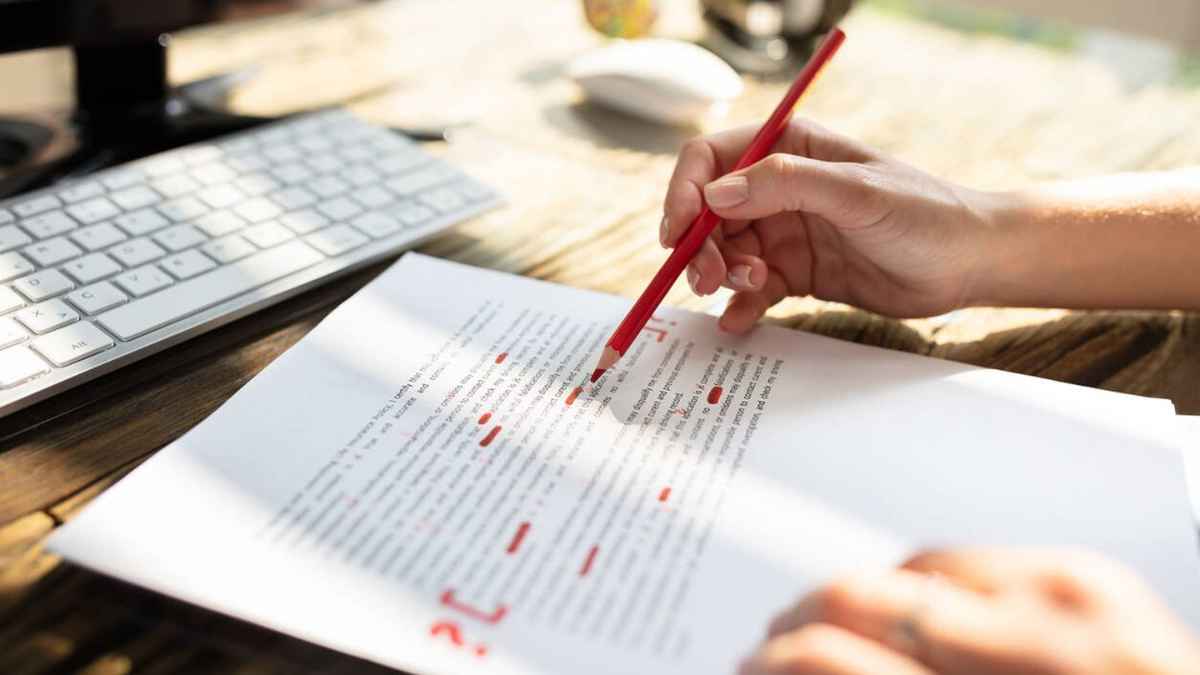 Profesora corrigiendo un examen con bolígrafo rojo sobre un escritorio de madera