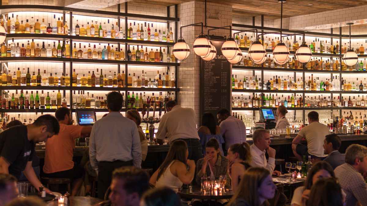 Prohibición Unión Europea envases monodosis interior de bar español con clientes y estanterías repletas de botellas, cafeterías y bares afectados