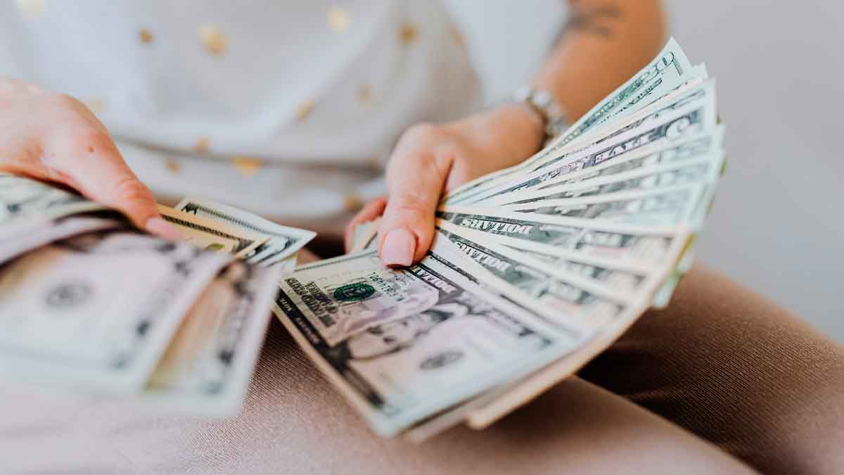 Manos sujetando un abanico de billetes de 100 $ que ilustra el aumento del salario mínimo en California 2025