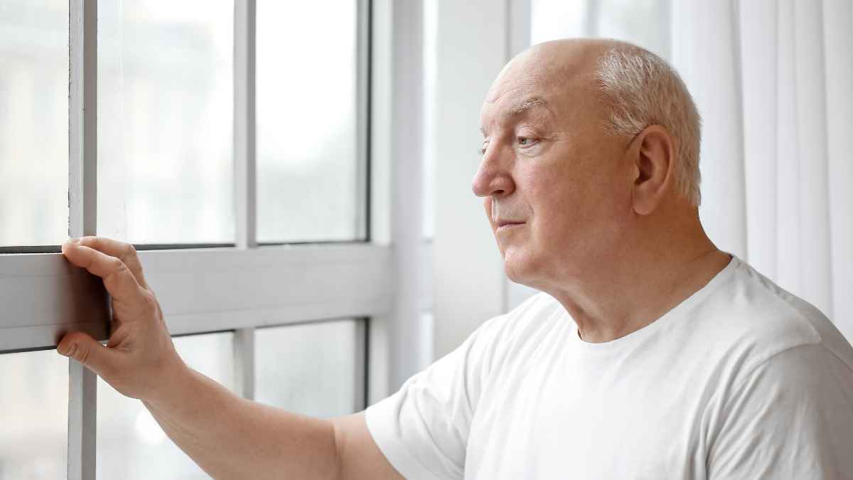 Hombre de 63 años mira pensativo por la ventana tras ganar al INSS y obtener una pensión de 2 .932 € mensuales