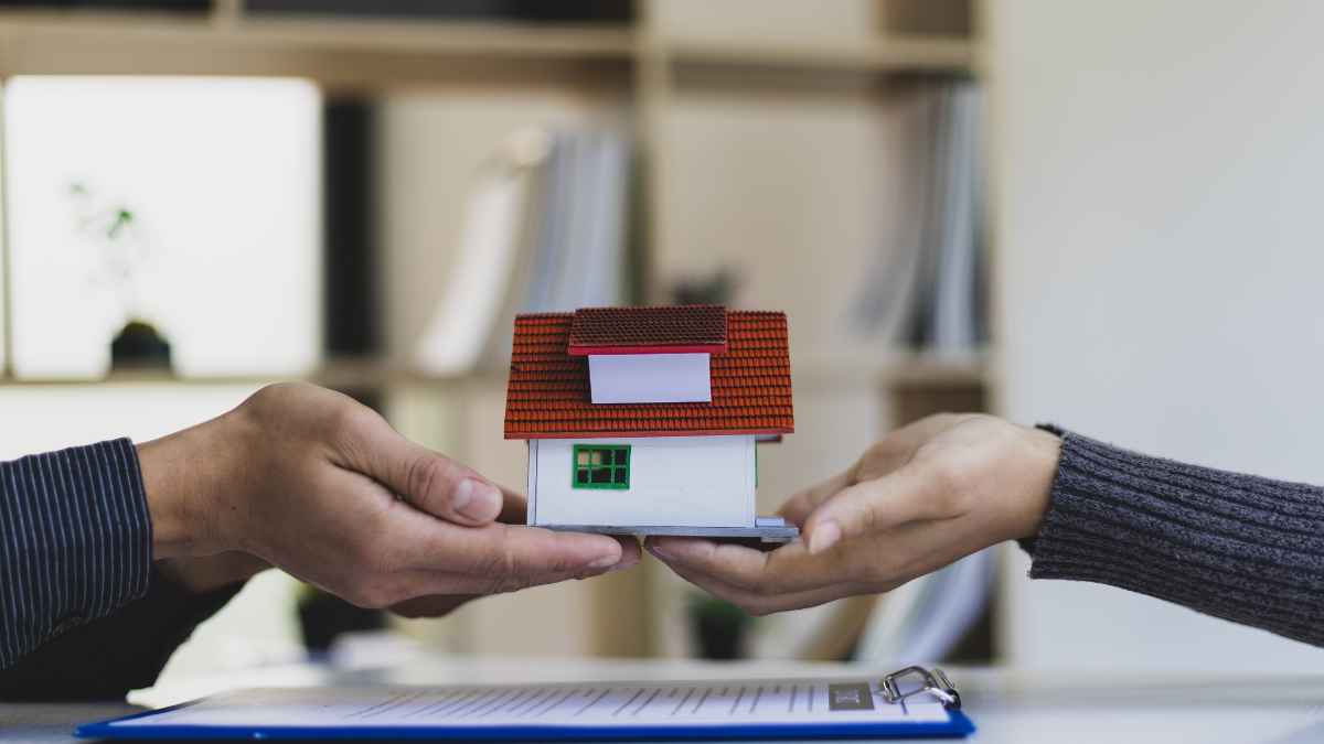 Dos manos intercambian una maqueta de casa, símbolo de repartir una vivienda en herencia entre varios hijos