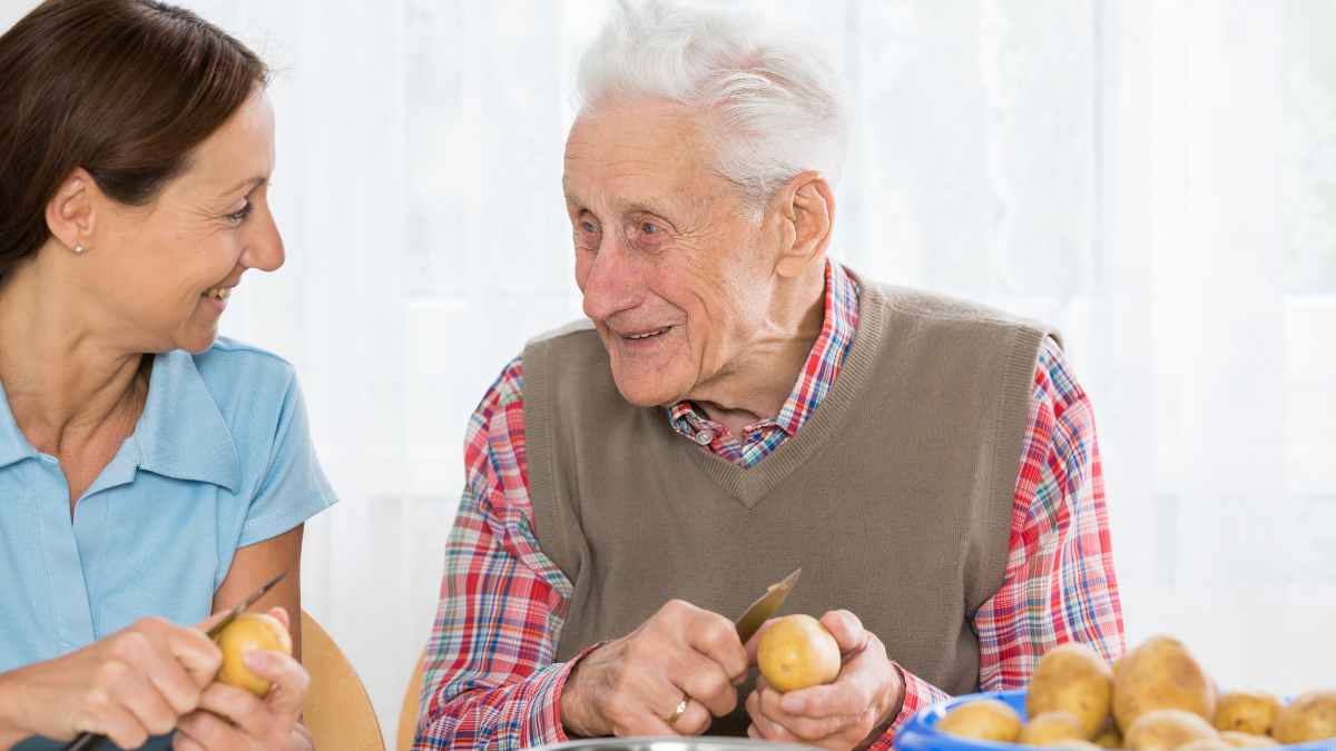 Hombre mayor pelando patatas junto a su acompañante, hobby de cocina creativo para mayores de 65 años