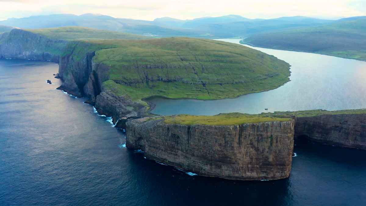 Vista aérea del lago Sørvágsvatn flotando 32 m sobre el océano Atlántico en las Islas Feroe, rodeado de acantilados verdes.