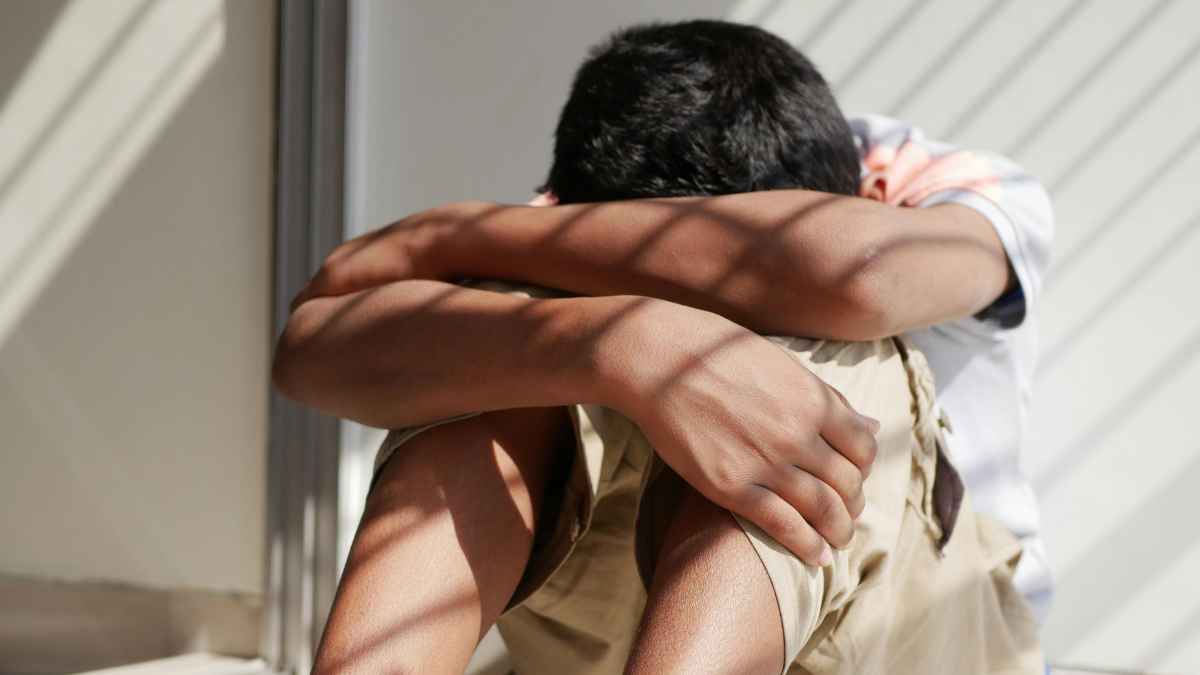 Niño cabizbajo sentado con los brazos sobre las rodillas, reflejando la ansiedad por la posible expulsión migratoria