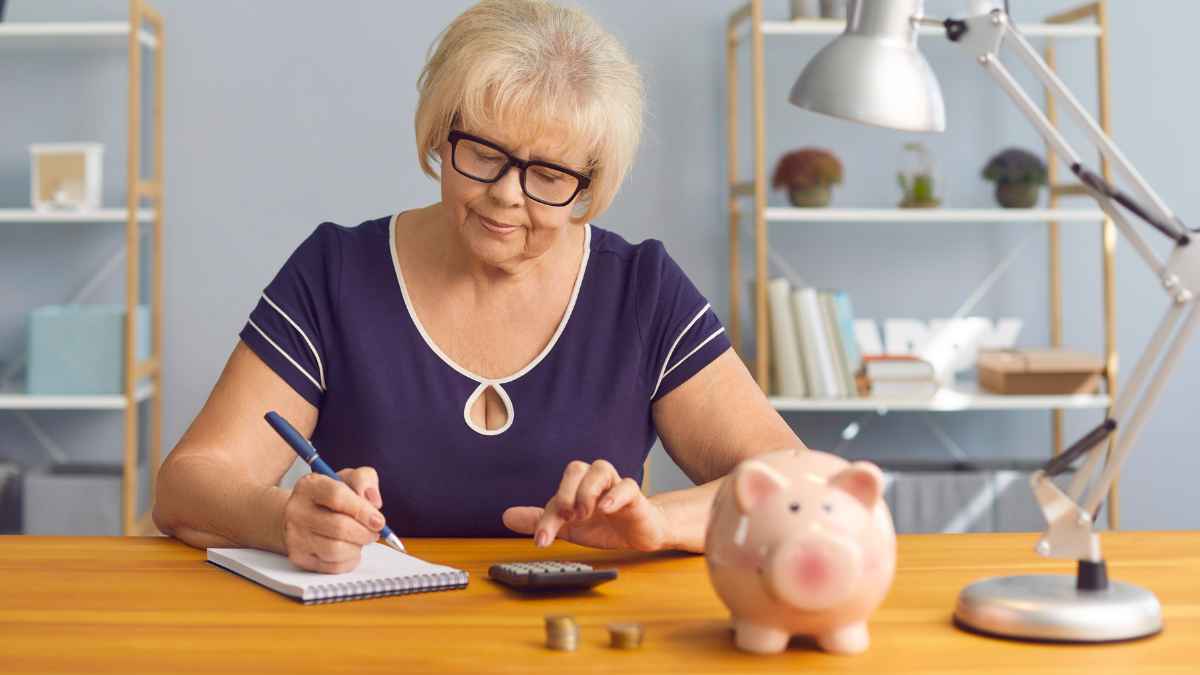 Mujer calculando su pensión con una calculadora y una hucha tras sumar hasta 5 años de cotización por prácticas sin cotizar