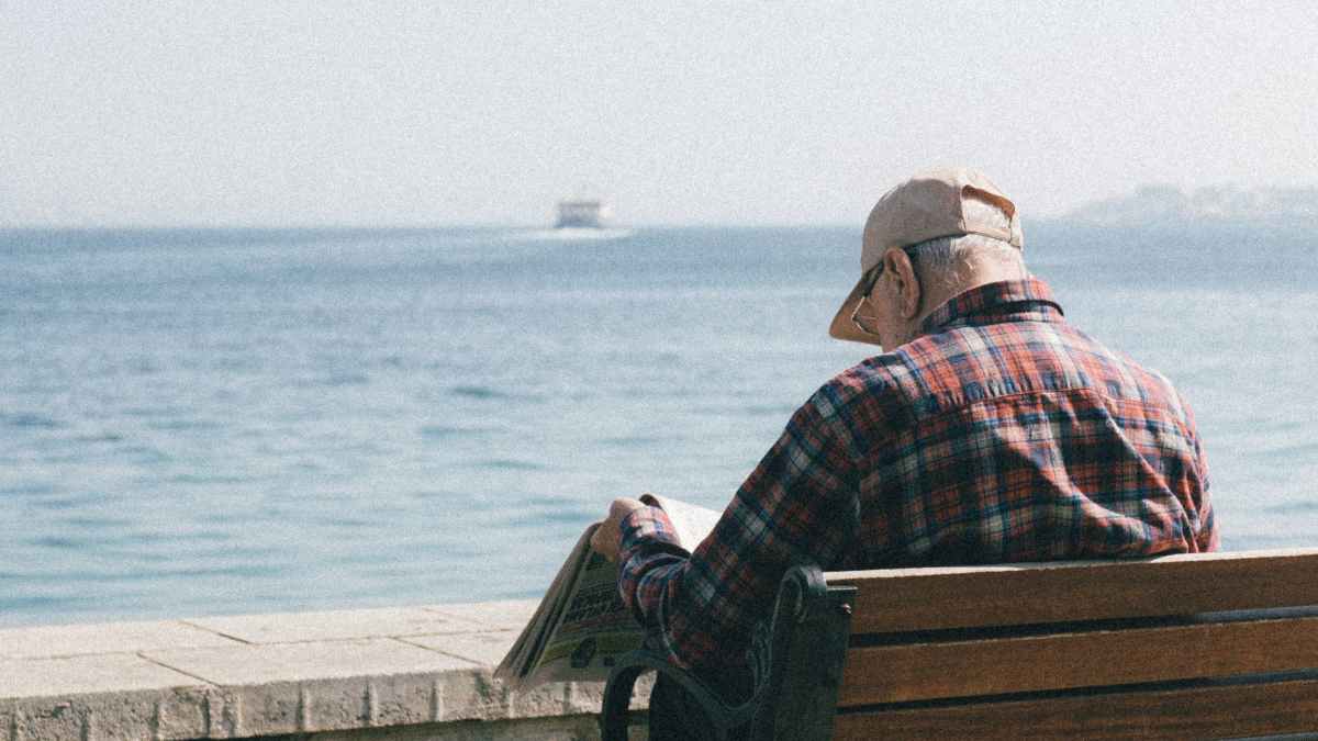 Funcionario jubilado leyendo un periódico frente al mar tras retrasar la jubilación hasta los 70 años