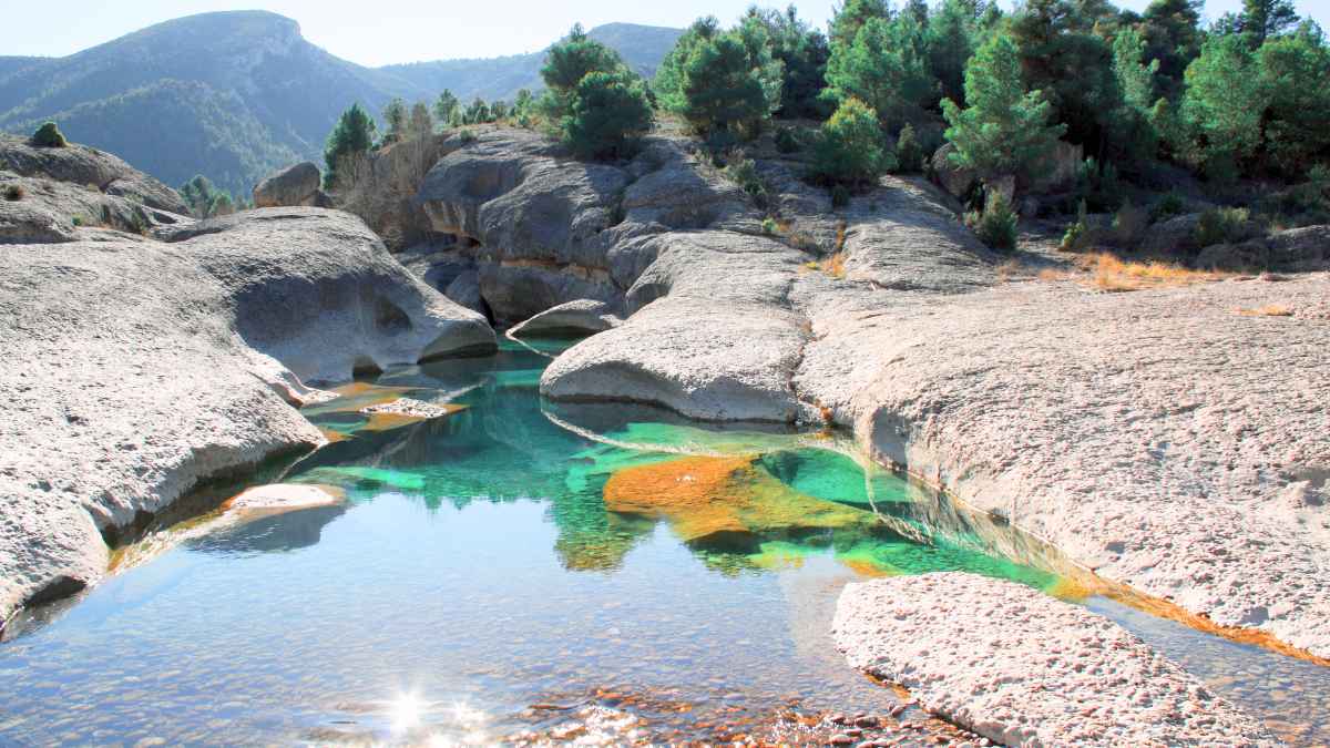 Piscina natural de agua turquesa en Aguaviva, Teruel, rodeada de rocas esculpidas y pinares del río Bergantes