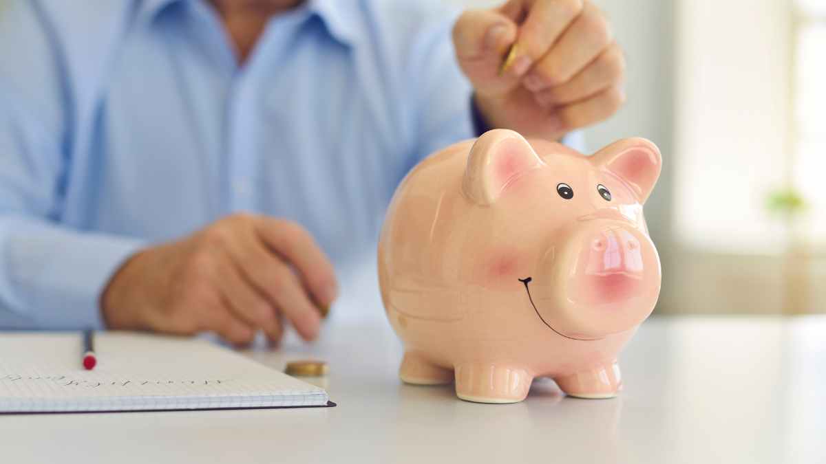 Persona introduce una moneda en una hucha cerdito que simboliza la pensión no contributiva de 7.905 € al año