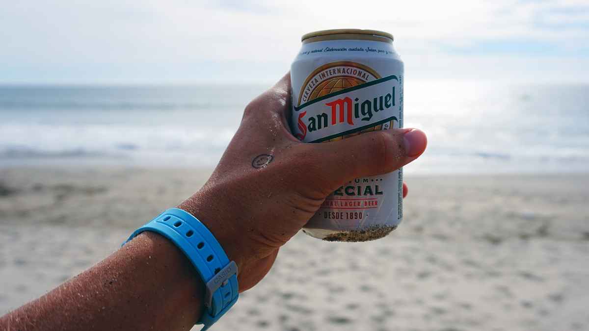 Persona bebiendo cerveza directamente de la lata en la playa