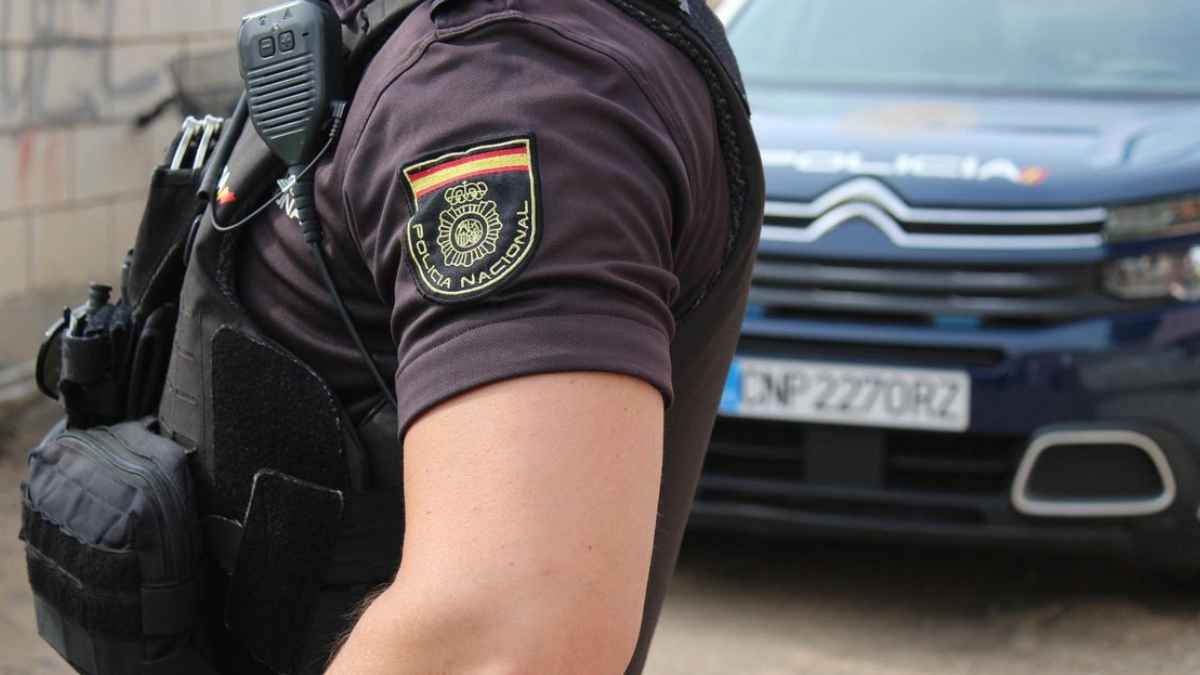 Agente y vehículo de la Policía Nacional, que alerta sobre la estafa telefónica con falsas ofertas de empleo
