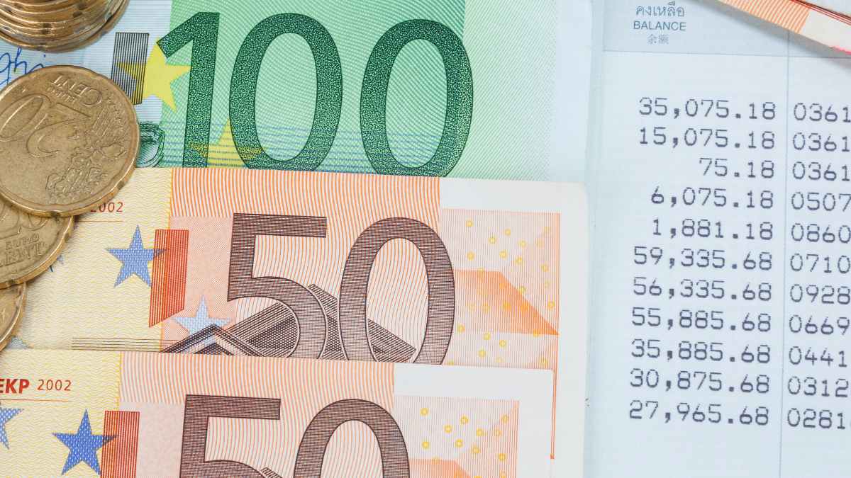 Billetes y monedas de euro junto a libreta bancaria mostrando saldo, representando cotitularidad de cuentas e implicaciones fiscales según Hacienda
