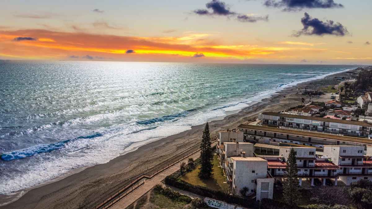 Vista aérea de la playa tranquila de Manilva en la Costa del Sol con el mar Mediterráneo y el atardecer.