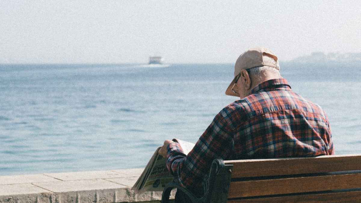 Hombre jubilado sentado en un banco frente al mar consultando información sobre jubilación anticipada involuntaria