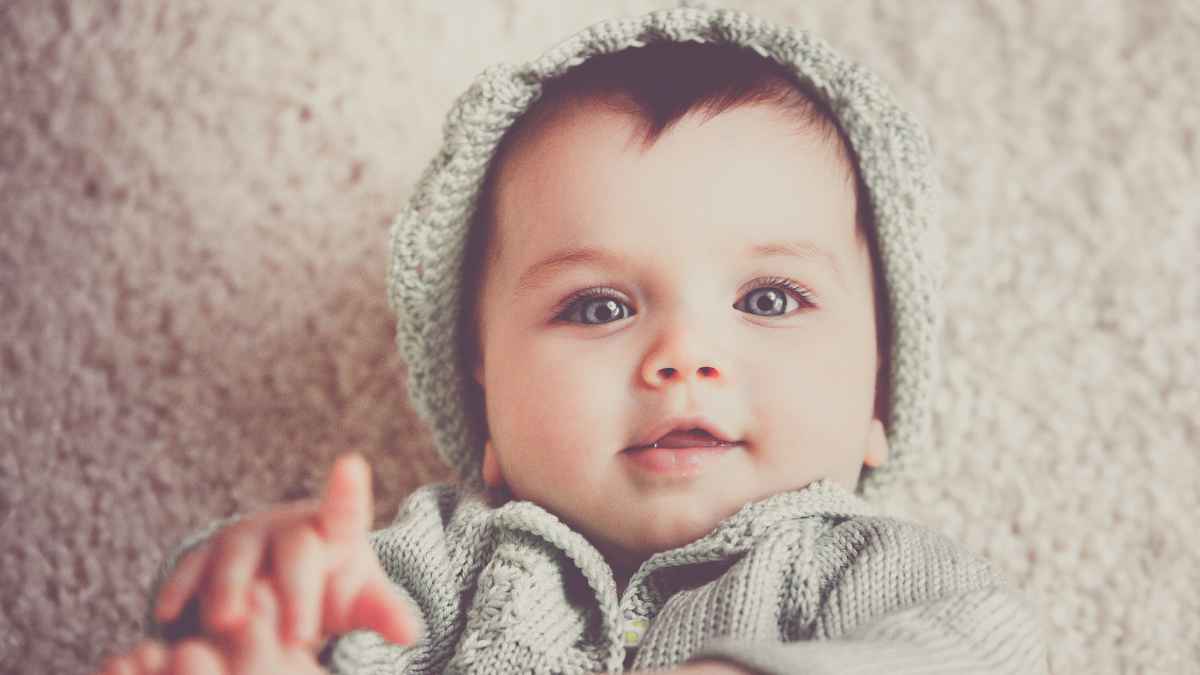 Bebé con jersey gris acostado sobre una manta, representando al nombre de niño más bonito según la ciencia