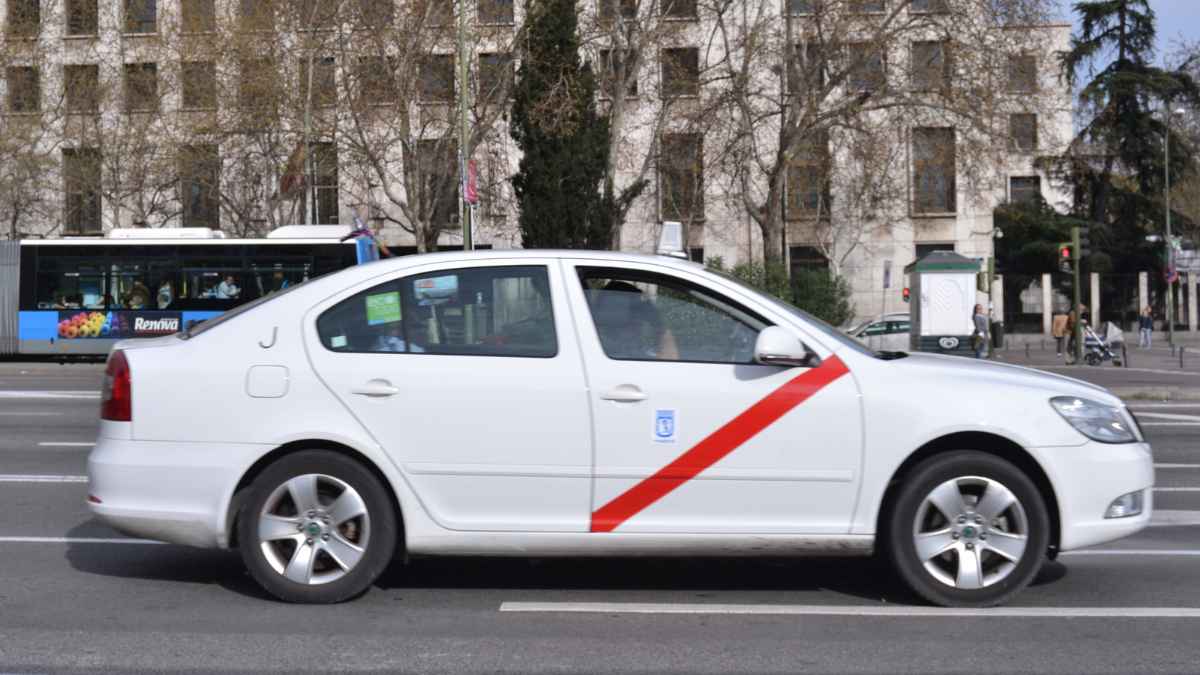 Taxi blanco circulando por Madrid, ciudad que cambia los requisitos para ser taxista eliminando la prueba del callejero
